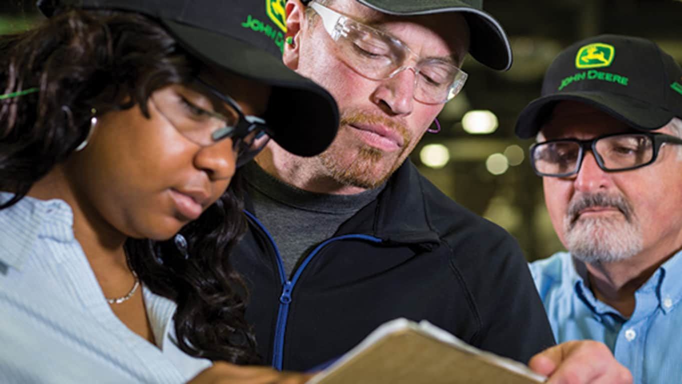 En gruppe John Deere-ansatte med vernebriller ser på en skriveplate