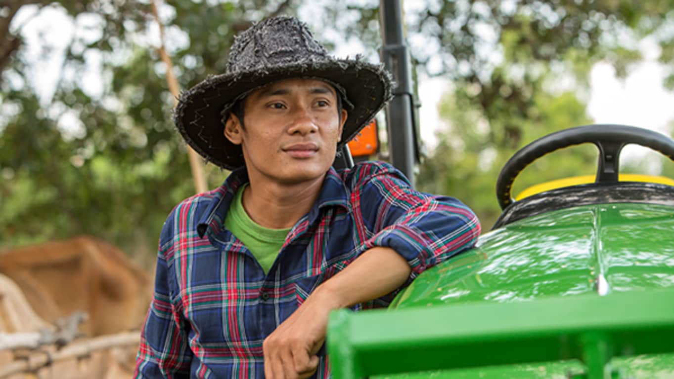 En mann med hatt står ved siden av sin John Deere-traktor