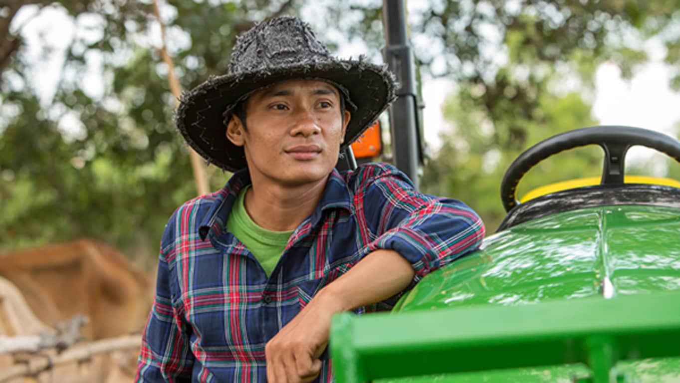 En mann med hatt står ved siden av sin John Deere-traktor