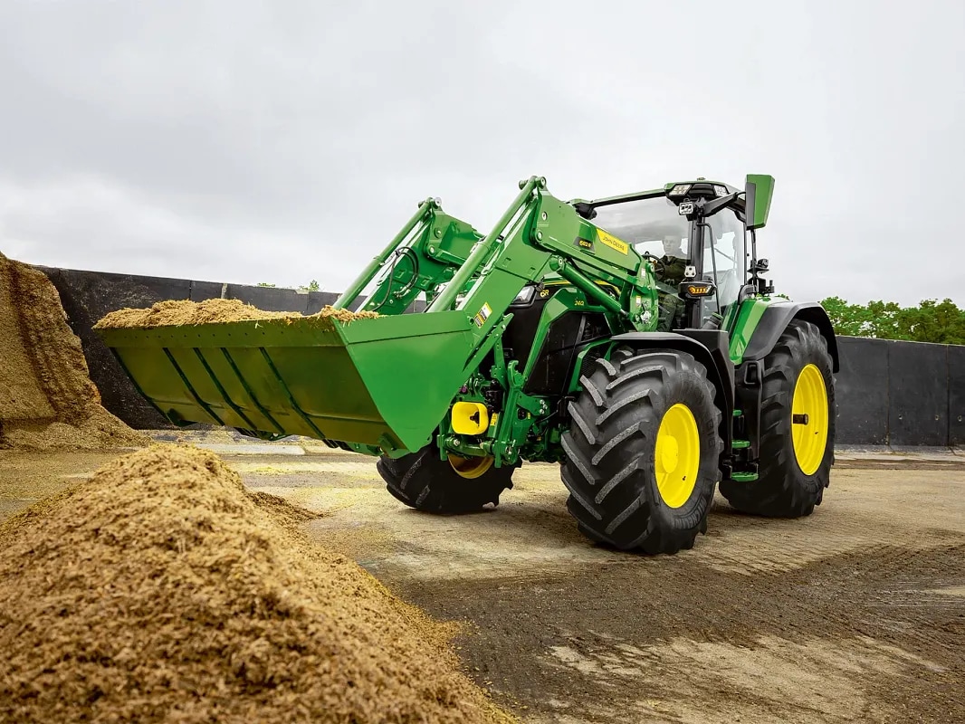 Frontlasteskuffe fylt med silofôr på en John Deere-traktor under materialhåndteringsarbeid.