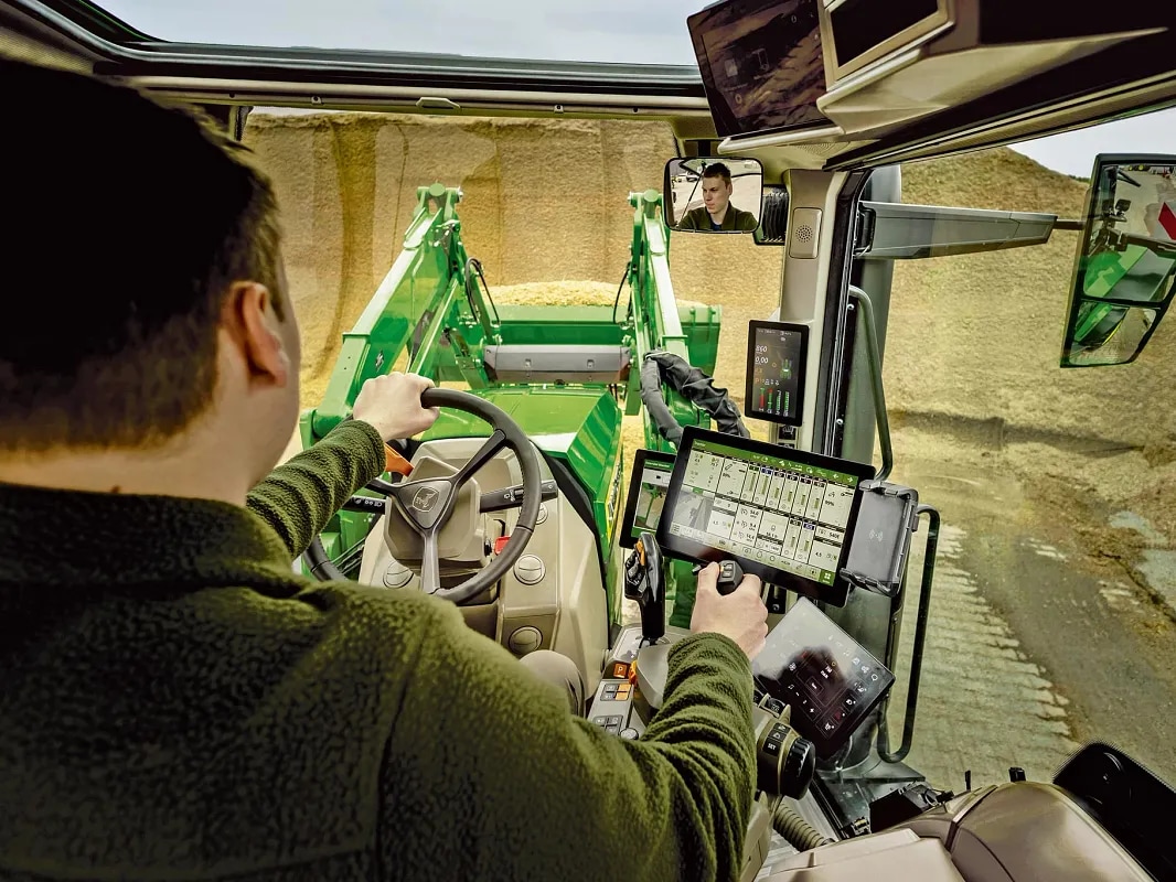 Utsikt fra førerhytten på John Deere-traktoren, som viser operatørkontroller og frontlasterdrift.