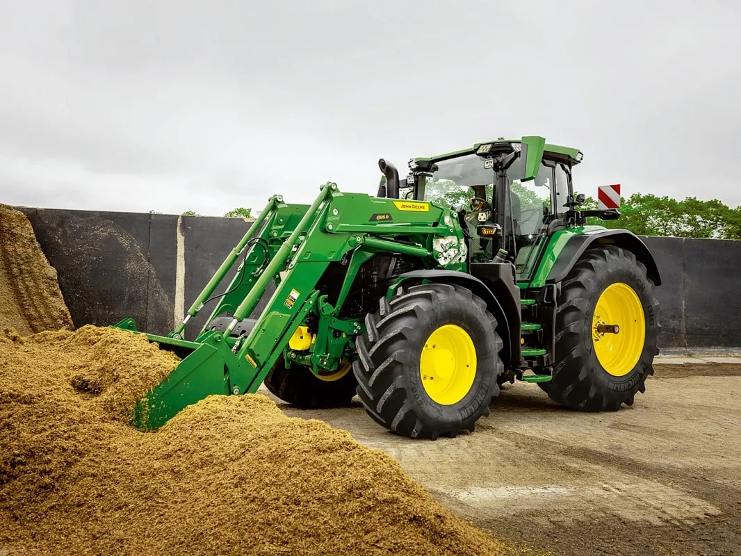 John Deere-traktor skyver inn i en silofôrhaug med frontlasterskuffe i landbruksmiljø.