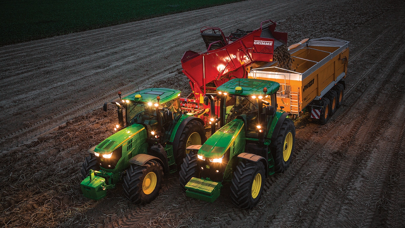 Traktoren som trekker h&oslash;stemaskinen fo poteter om kvelden t&oslash;mmer potetene i en vogn som dras av en annen traktor.