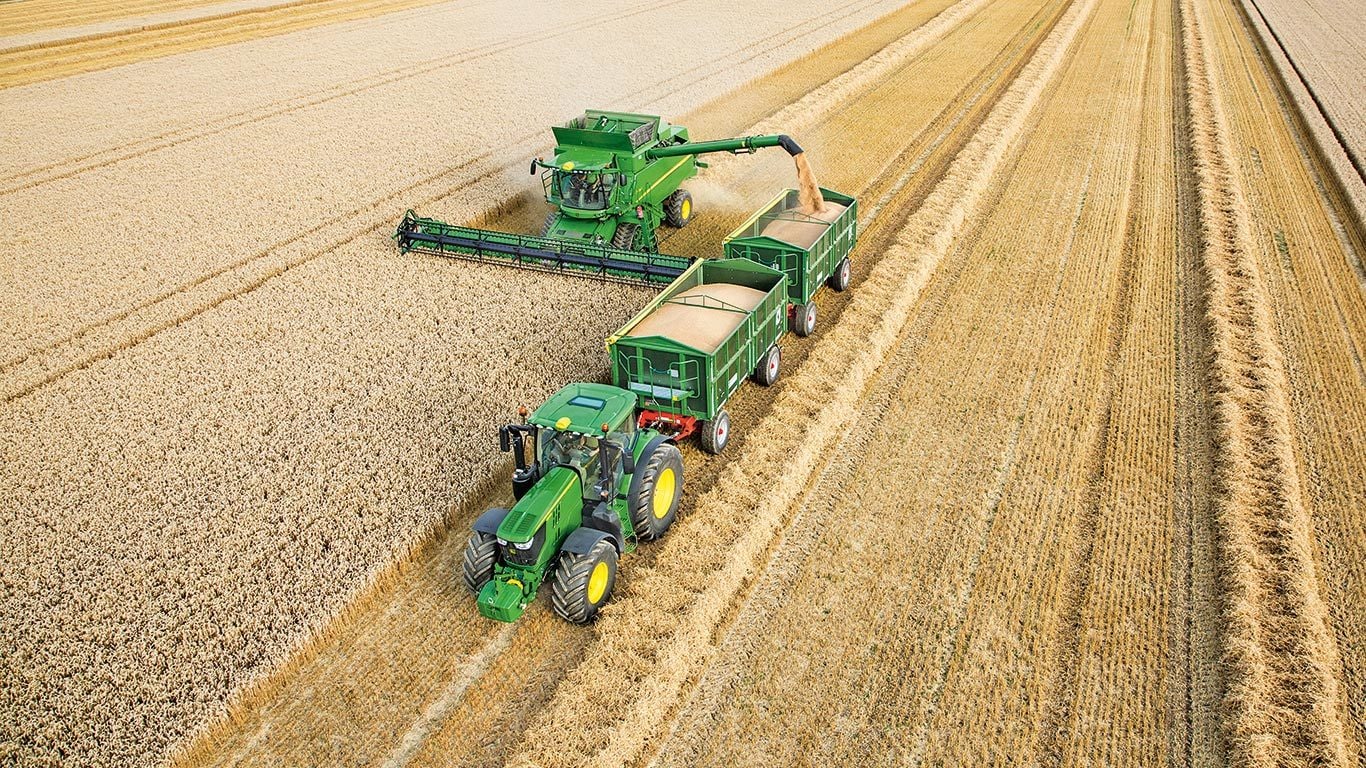 John Deere&trade; skurtresker i S-serien som losser hvete i doble tilhengere som trekkes av traktor