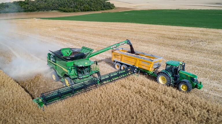 John Deere&trade; skurtresker i X-serien som losser rapsfr&oslash; i en kornvogn som trekkes av en John Deere&trade; traktor