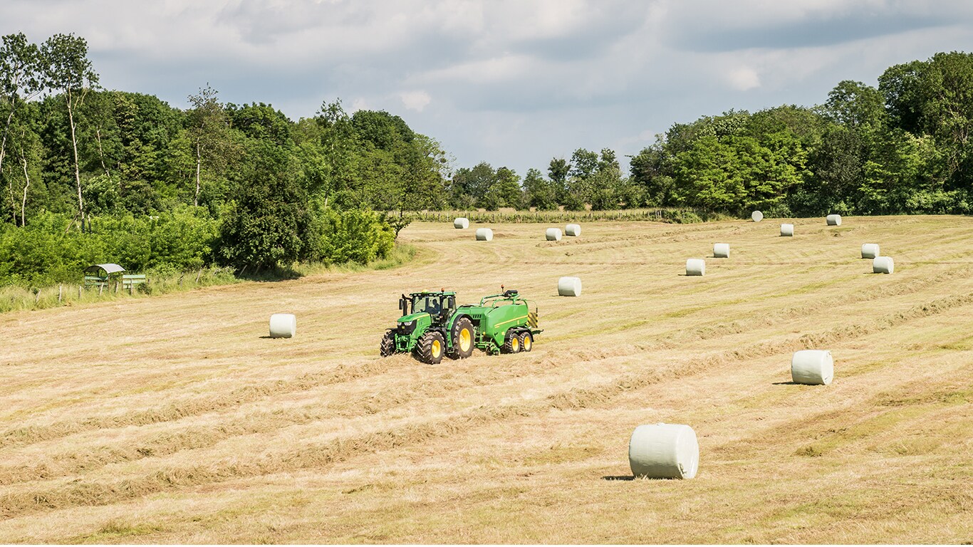 John Deere™ traktor med rundballepresse på åkeren med rundballer med silofôr