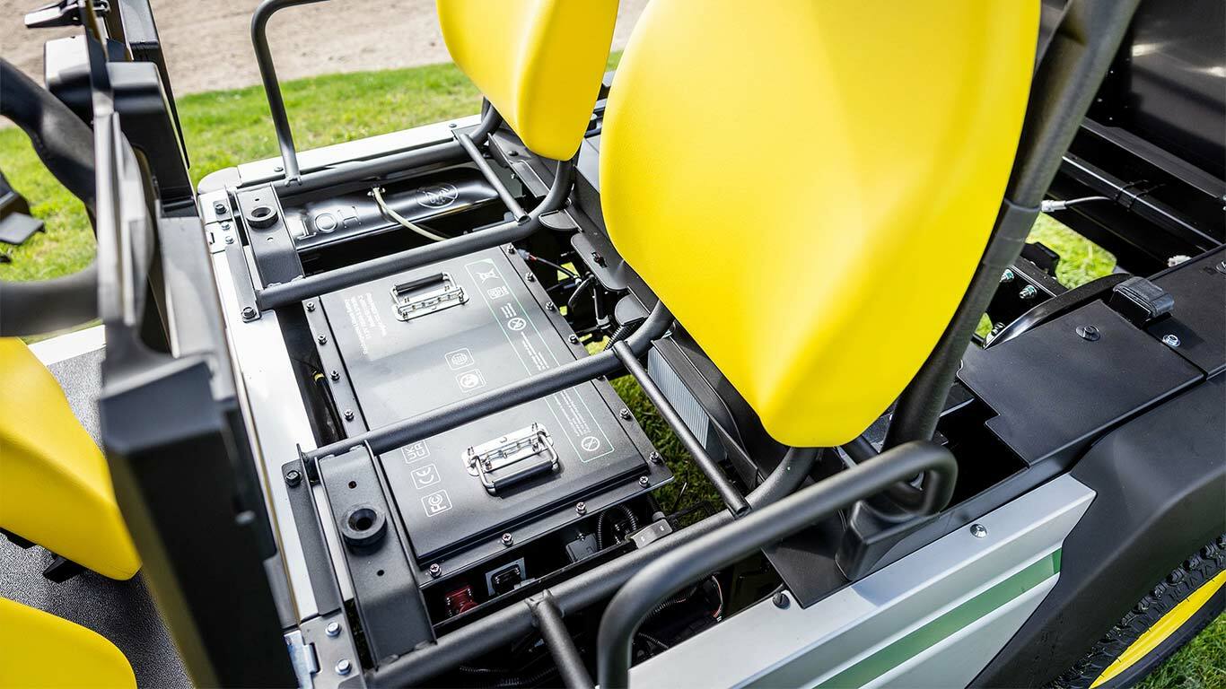 Nærbilde av to litium-batteripakker montert under lyse gule seter i et elektrisk nyttekjøretøy fra John Deere Gator GS.
