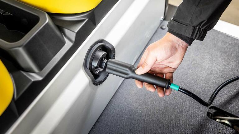 Hånd som setter en ladekabel inn i sideporten på et elektrisk nyttekjøretøy fra John Deere Gator GS.