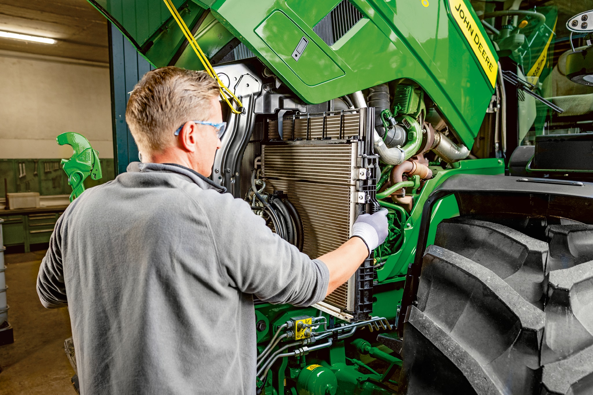 Servicetekniker utfører vedlikehold inne i motorrommet på en John Deere-traktor i 6M-serien.