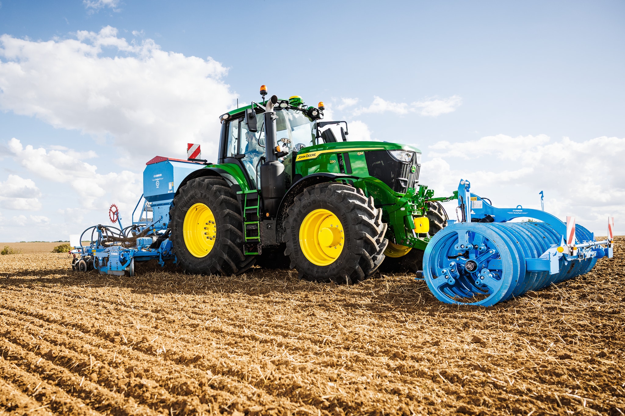 John Deere-traktor i 6M-serien dyrker en åker med en stor blå rulle montert.