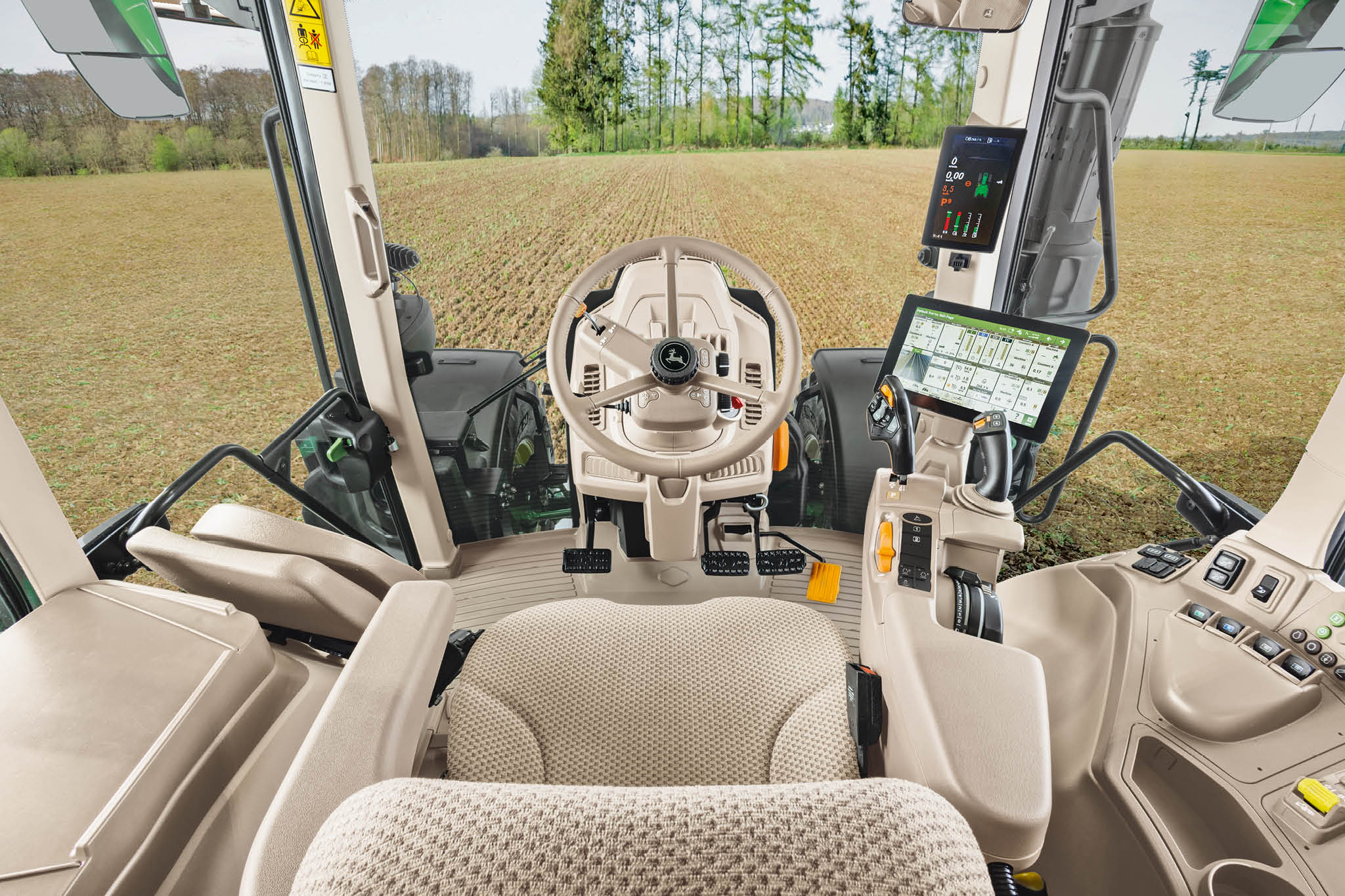 Interiøroversikt over en førerhytte i John Deere 6M-serien med førersete, ratt og digitale displayer.
