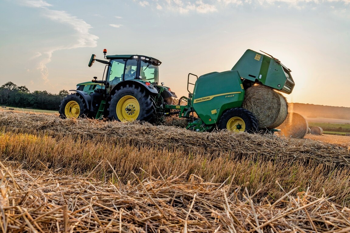John Deere F442M-ballepresse trukket av en John Deere 6M-traktor som kaster ut en halmballe