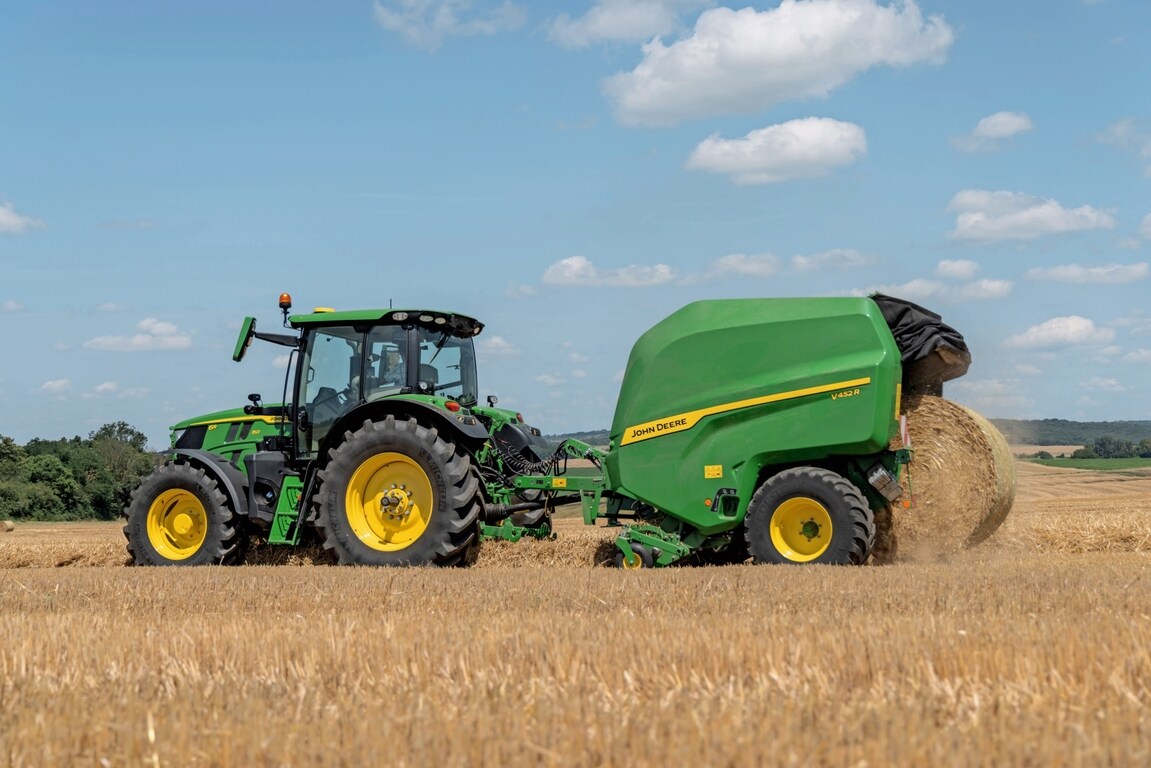 John Deere V452R i en stråmark trukket av en John Deere 6R 150 som kaster ut en balle
