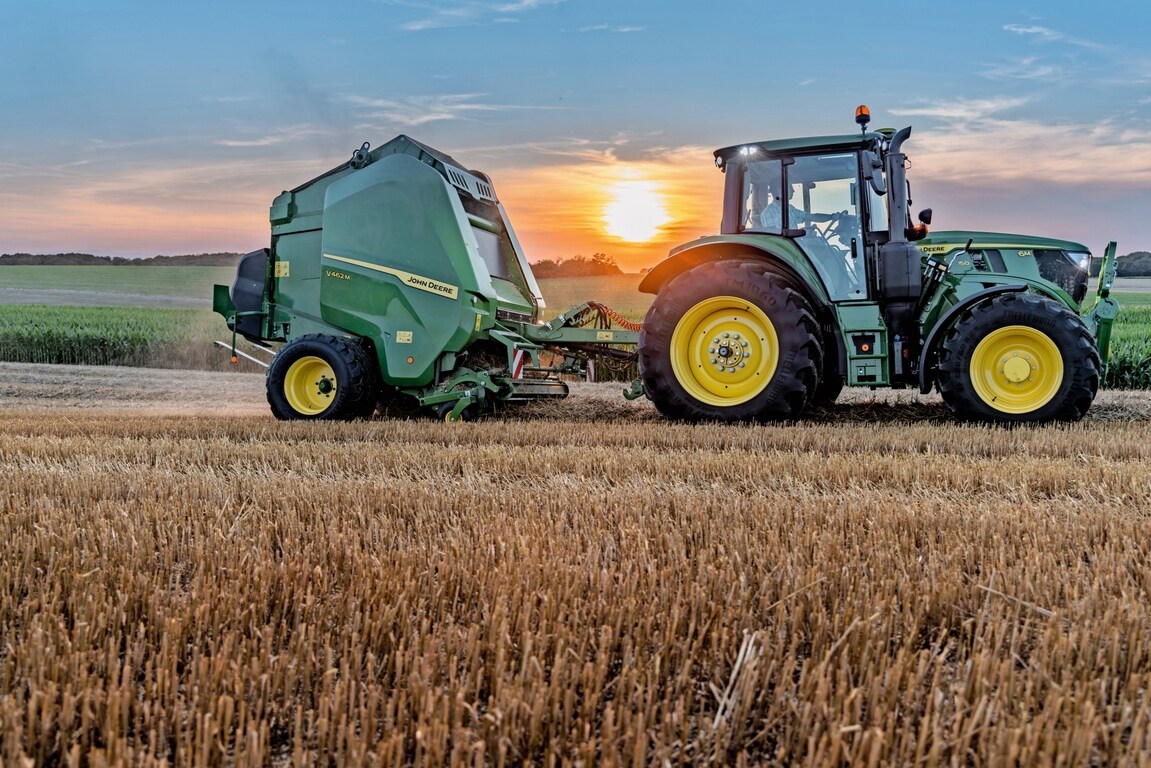 John Deere V462M i en stråmark trukket av en John Deere 6M 150 ved solnedgang