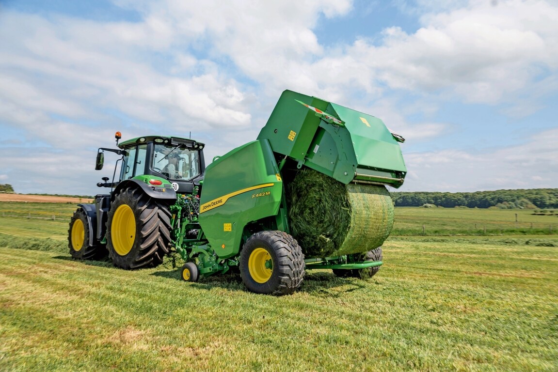 John Deere F442M-ballepresse trukket av en John Deere 6M-traktor som kaster ut en gressballe