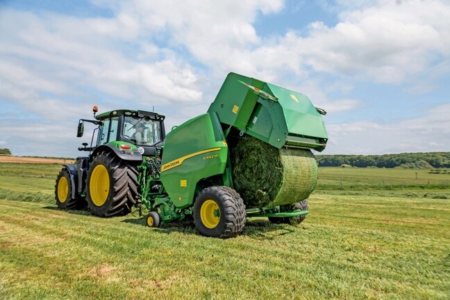 John Deere F442M-ballepresse trukket av en John Deere 6M-traktor som kaster ut en gressballe