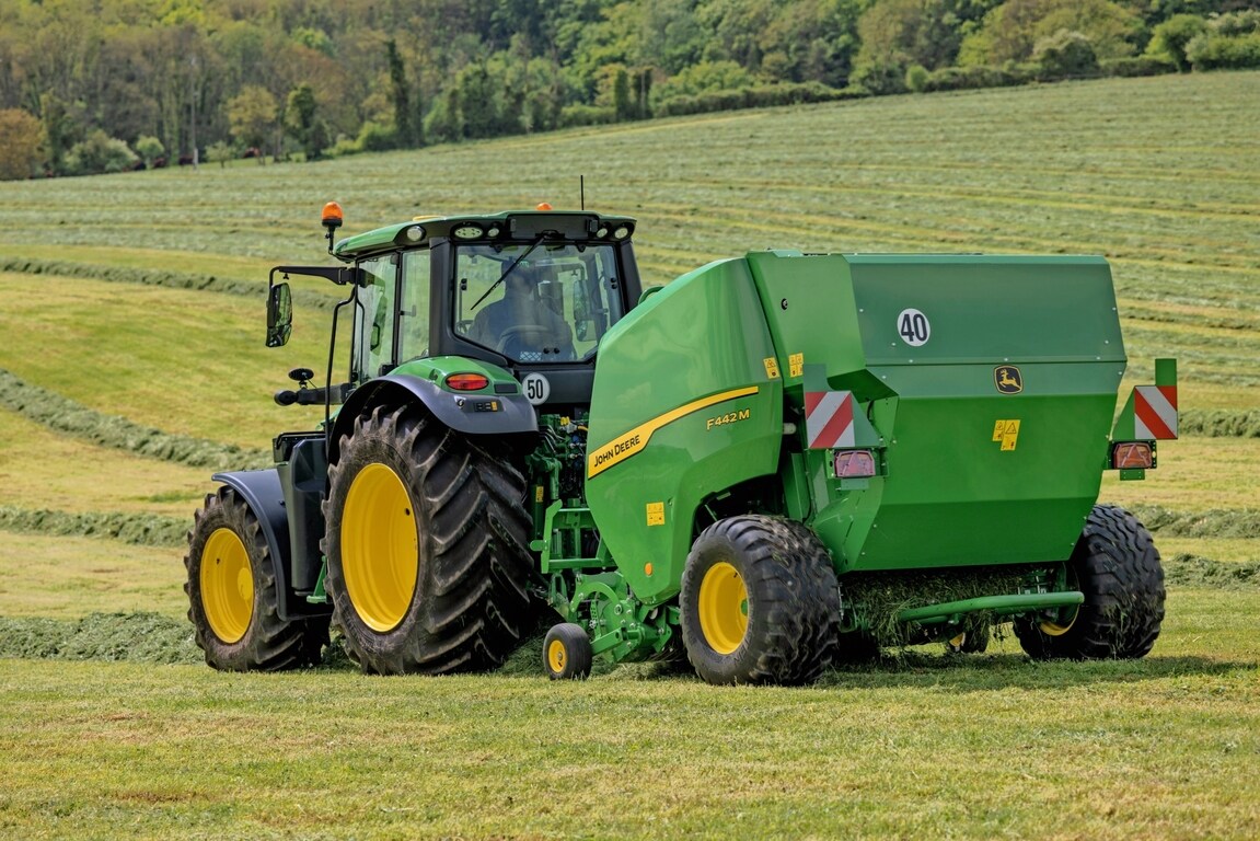 John Deere F442M-ballepresse trukket av en John Deere 6M-traktor på en kupert gressmark