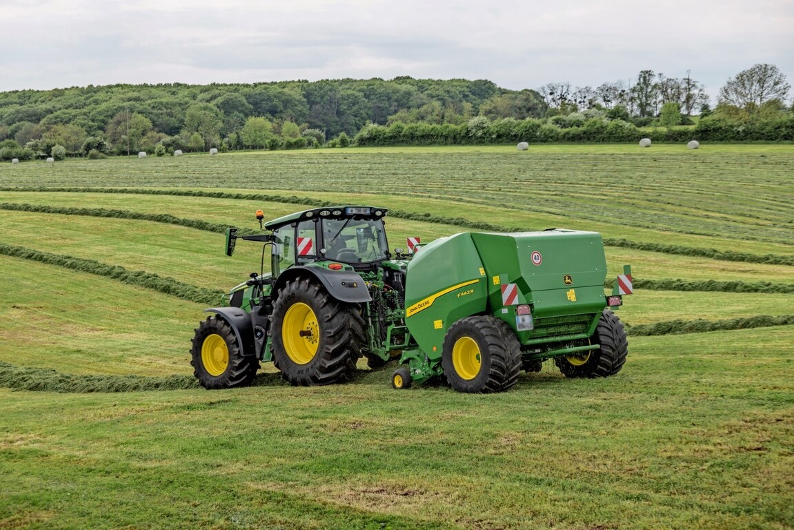 John Deere F442R-ballepresse trukket av en John Deere 6M-traktor på en kupert mark