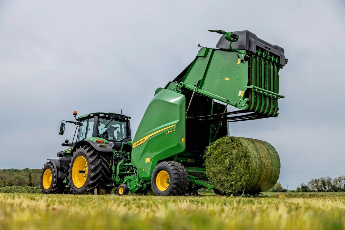 John Deere V462M-ballepresse trukket av en John Deere 6M-traktor som kaster ut en gressballe