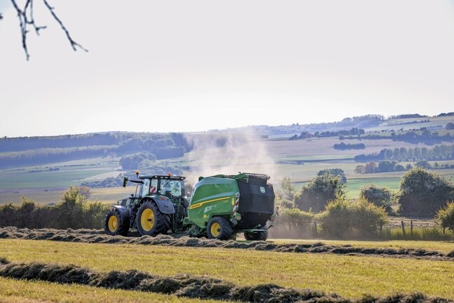 John Deere V462R trukket av en John Deere 6R 185-traktor for rundballepressing av høy